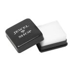 Picture of opened charm box, A small square black plastic box with slightly rounded corners and sparkling silver bits embedded in the material. The pull-off lid features the words "Jewel Shop" in white print at the top. The inside is lined with white cotton wool.