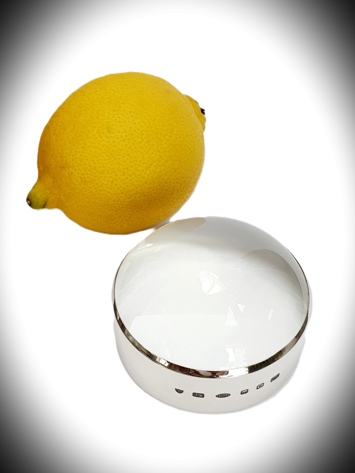Spotlight effect on sterling silver surround, paired with glass dome—feature hallmark not visible, showcasing minimalist styling. Pictured next to a lemon for comparison.
