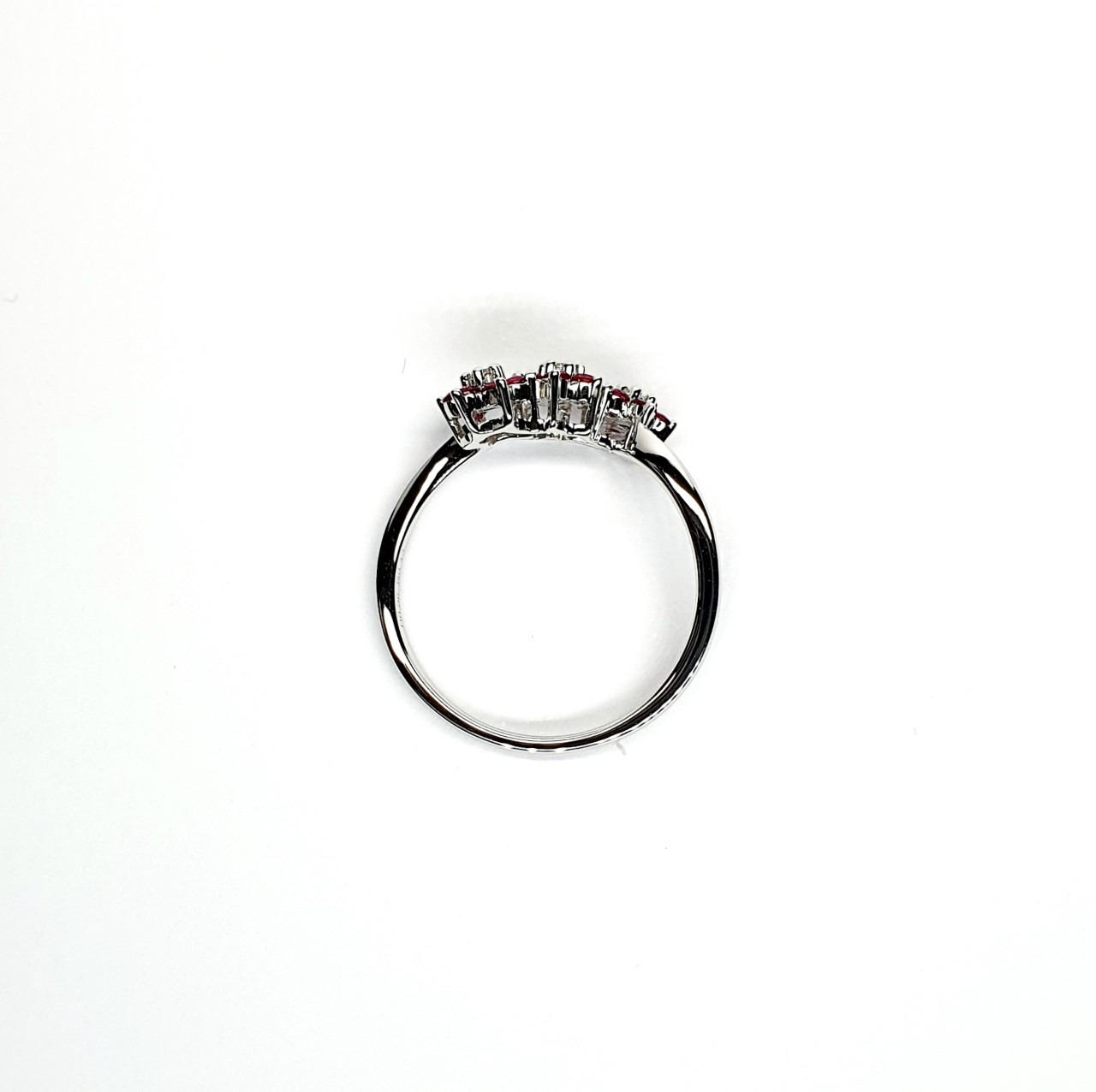 A captivating image of a Three Cluster Ruby Ring in 18ct white gold. The ring showcases three clusters of vibrant rubies, with six rubies in each cluster. Adorning the ring shank is a graceful wave design, adding a touch of elegance to the overall aesthetic. The clusters are accentuated by three sparkling diamonds, positioned at the centre of each cluster." Side view.