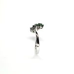 A captivating image of a Three Cluster Emerald Ring in 18ct white gold. The ring showcases three clusters of vibrant green emeralds, with six emeralds in each cluster. Adorning the ring shank is a graceful wave design, adding a touch of elegance to the overall aesthetic. The clusters are accentuated by three sparkling diamonds, positioned at the centre of each cluster." Edge view.