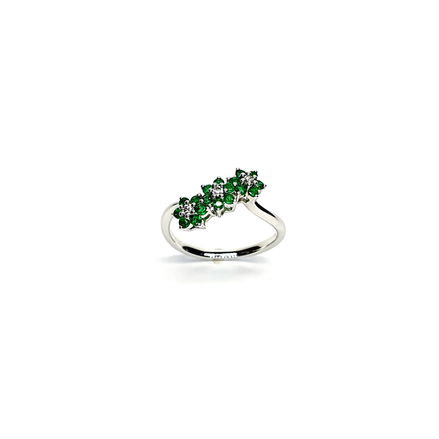A captivating image of a Three Cluster Emerald Ring in 18ct white gold. The ring showcases three clusters of vibrant green emeralds, with six emeralds in each cluster. Adorning the ring shank is a graceful wave design, adding a touch of elegance to the overall aesthetic. The clusters are accentuated by three sparkling diamonds, positioned at the centre of each cluster." Angled top view.