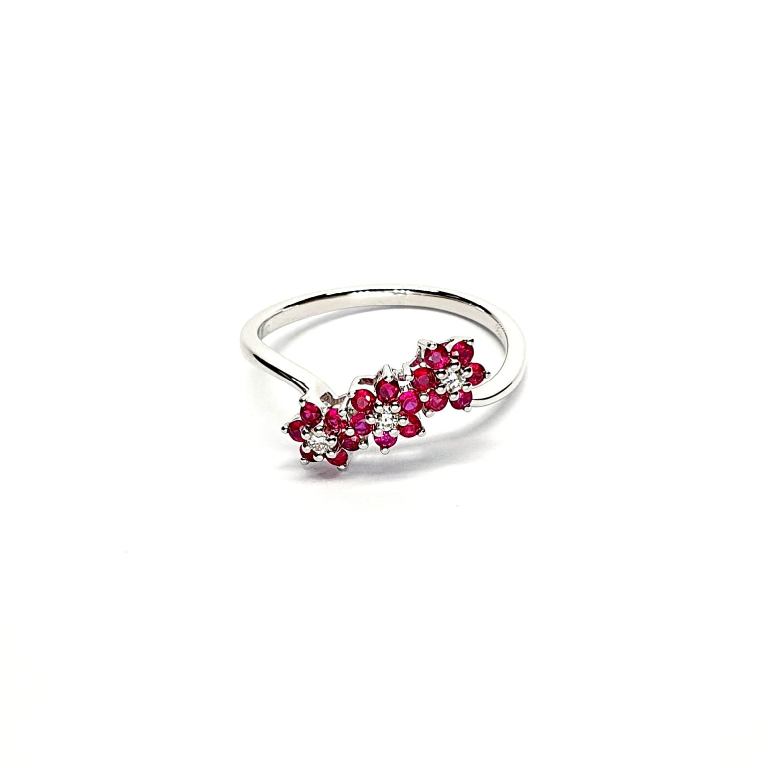A captivating image of a Three Cluster Ruby Ring in 18ct white gold. The ring showcases three clusters of vibrant rubies, with six rubies in each cluster. Adorning the ring shank is a graceful wave design, adding a touch of elegance to the overall aesthetic. The clusters are accentuated by three sparkling diamonds, positioned at the centre of each cluster." Lying flat view.