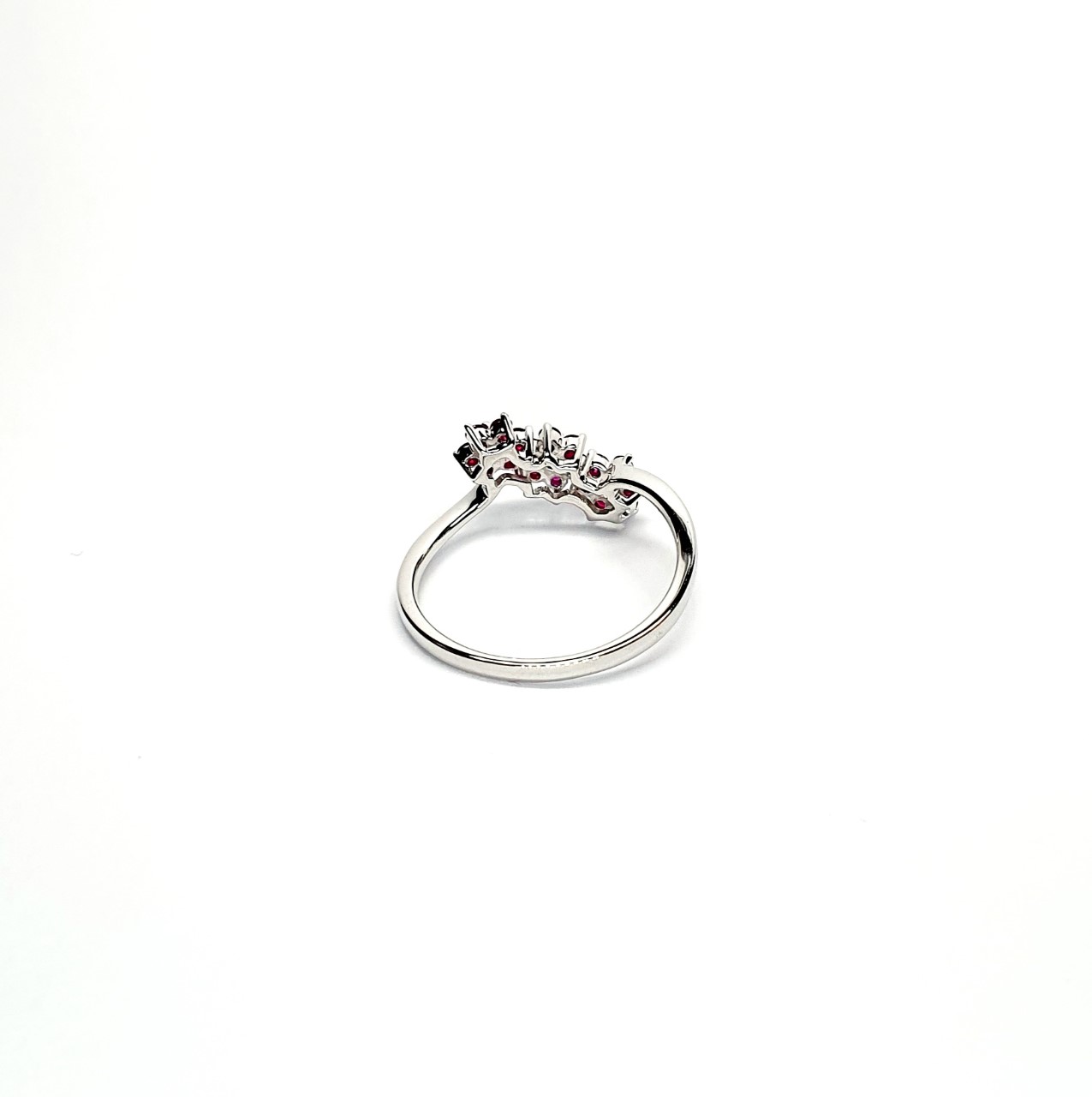 A captivating image of a Three Cluster Ruby Ring in 18ct white gold. The ring showcases three clusters of vibrant rubies, with six rubies in each cluster. Adorning the ring shank is a graceful wave design, adding a touch of elegance to the overall aesthetic. The clusters are accentuated by three sparkling diamonds, positioned at the centre of each cluster." Back view.