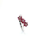 A captivating image of a Three Cluster Ruby Ring in 18ct white gold. The ring showcases three clusters of vibrant rubies, with six rubies in each cluster. Adorning the ring shank is a graceful wave design, adding a touch of elegance to the overall aesthetic. The clusters are accentuated by three sparkling diamonds, positioned at the centre of each cluster." Angled top view.