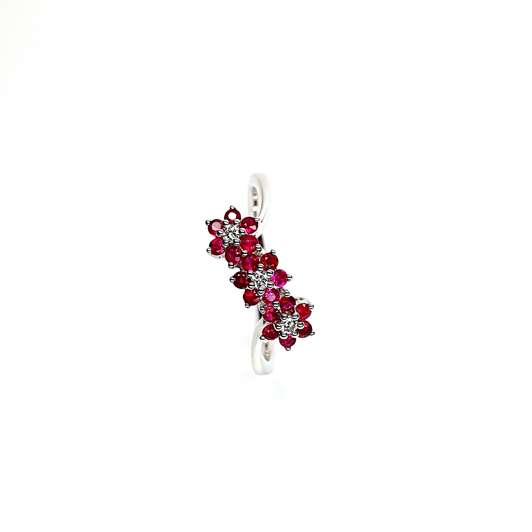 A captivating image of a Three Cluster Ruby Ring in 18ct white gold. The ring showcases three clusters of vibrant rubies, with six rubies in each cluster. Adorning the ring shank is a graceful wave design, adding a touch of elegance to the overall aesthetic. The clusters are accentuated by three sparkling diamonds, positioned at the centre of each cluster." Top view.