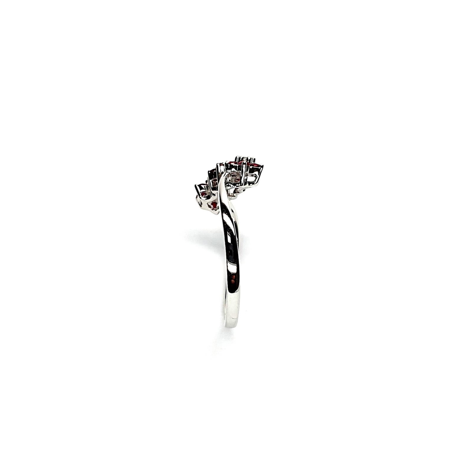 A captivating image of a Three Cluster Ruby Ring in 18ct white gold. The ring showcases three clusters of vibrant rubies, with six rubies in each cluster. Adorning the ring shank is a graceful wave design, adding a touch of elegance to the overall aesthetic. The clusters are accentuated by three sparkling diamonds, positioned at the centre of each cluster." Edge view.