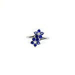 "An elegant 18ct white gold ring with a crossover shank featuring two clusters of five round bright blue sapphires, each cluster surrounds a single white sparkling diamond, creating a captivating and sophisticated design." Top View.