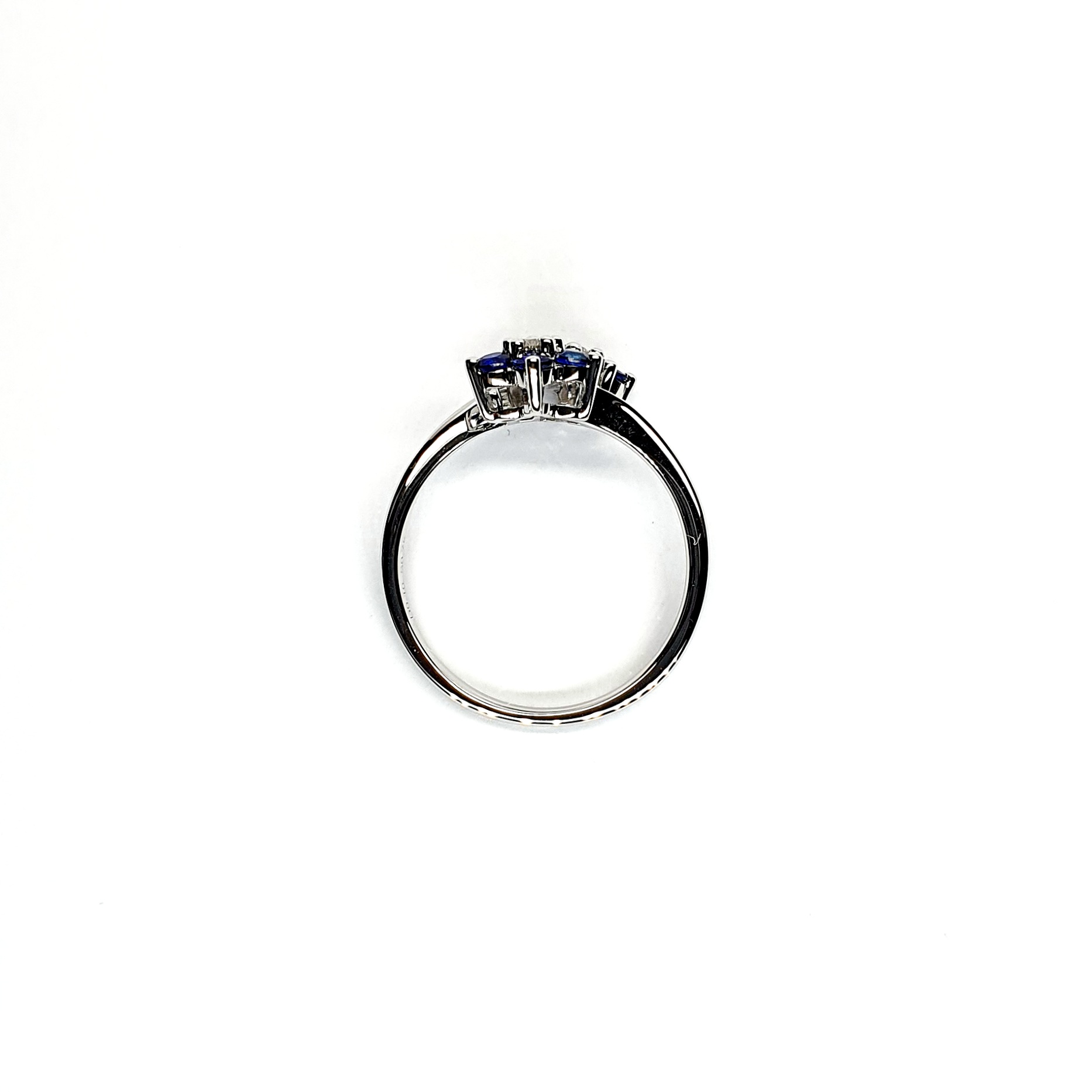 "An elegant 18ct white gold ring with a crossover shank featuring two clusters of five round bright blue sapphires, each cluster surrounds a single white sparkling diamond, creating a captivating and sophisticated design." Side View