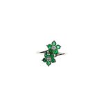 Double Cluster Emerald Ring. Crafted in 18ct white gold featuring two clusters of five round bright green emeralds with a single diamond to the centre of each cluster, with a wave cross over shank