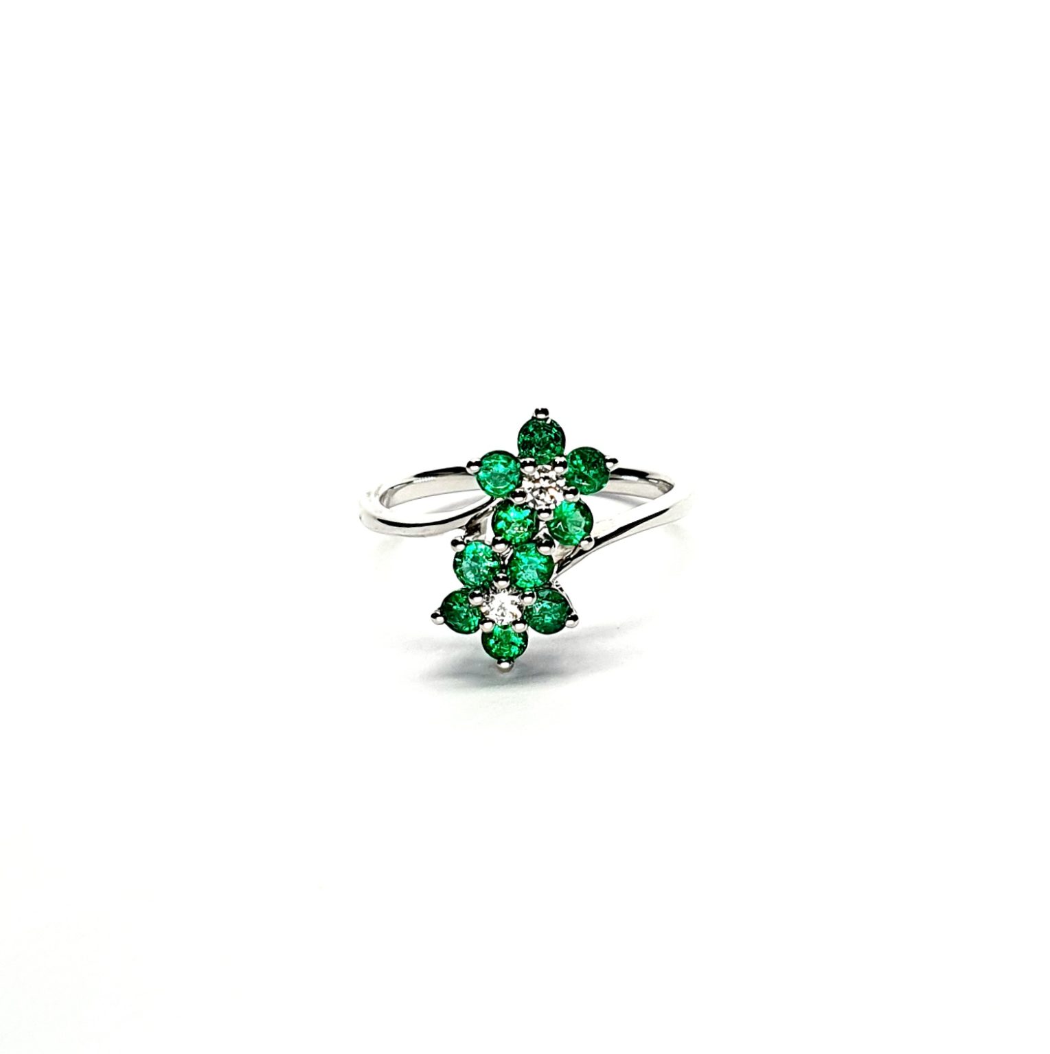 Double Cluster Emerald Ring. Crafted in 18ct white gold featuring two clusters of five round bright green emeralds with a single diamond to the centre of each cluster, with a wave cross over shank