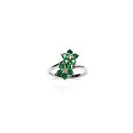 Double Cluster Emerald Ring. Crafted in 18ct white gold featuring two clusters of five round bright green emeralds with a single diamond to the centre of each cluster, with a wave cross over shank