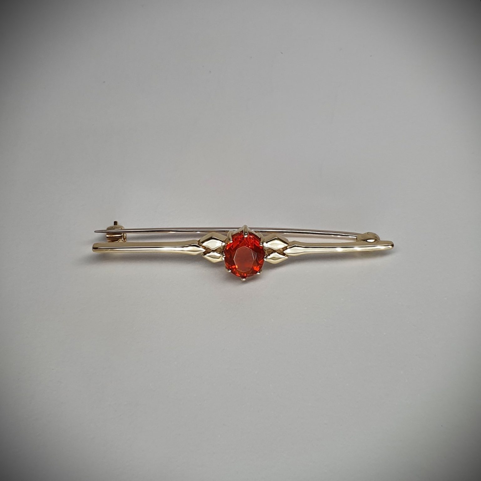 A handmade 9ct yellow gold bar brooch 52mm long set with a gorgeous top quality oval fire opal measuring 8.6mm x 7mm portrait set to the middle of the bar with three 9ct gold diamond shapes to each side of the stone with a straight pin to the back with a swivel safety catch.