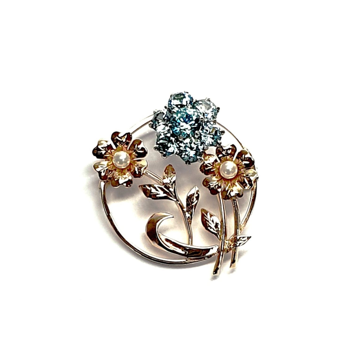 9ct Gold Blue Flower Brooch, three stems of flowers in a circle. In the centre is a flower with six round blue zircon petals set in white gold, with a six-petal 9ctyellow  gold flower on each side set with a single pearl to each centre.