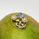 9ct Gold Blue Flower Brooch, three stems of flowers in a circle. In the centre is a flower with six round blue zircon petals set in white gold, with a six-petal 9ctyellow  gold flower on each side set with a single pearl to each centre.