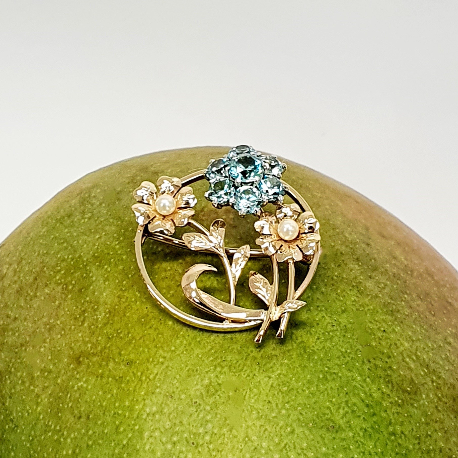 9ct Gold Blue Flower Brooch, three stems of flowers in a circle. In the centre is a flower with six round blue zircon petals set in white gold, with a six-petal 9ctyellow  gold flower on each side set with a single pearl to each centre.