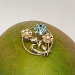 9ct Gold Blue Flower Brooch, three stems of flowers in a circle. In the centre is a flower with six round blue zircon petals set in white gold, with a six-petal 9ctyellow  gold flower on each side set with a single pearl to each centre.