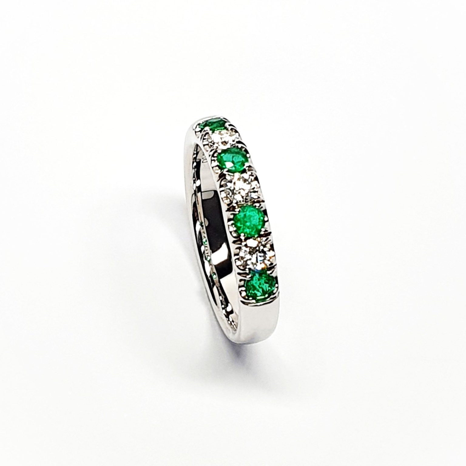 18ct White Gold Emerald & Diamond Eternity Ring RA00685 Four 2.8mm round emeralds and three 2.8mm round diamonds ring standing up to the front angled facing to the right. Close up with a white background