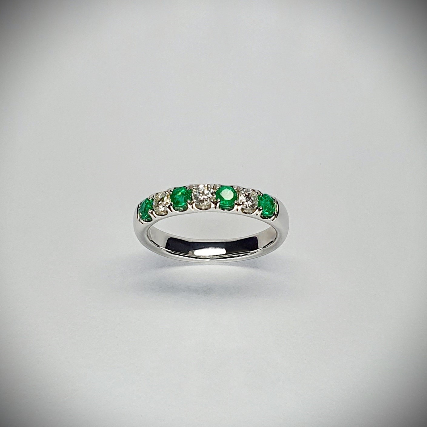 18ct White Gold Emerald & Diamond Eternity Ring RA00685 Four 2.8mm round emeralds and three 2.8mm round diamonds ring standing up to the front angled facing to the front. With a dark background.