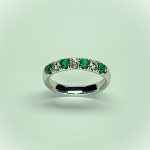 18ct White Gold Emerald & Diamond Eternity Ring RA00685 Four 2.8mm round emeralds and three 2.8mm round diamonds ring standing up to the front angled facing to the front. With a green tinted background.