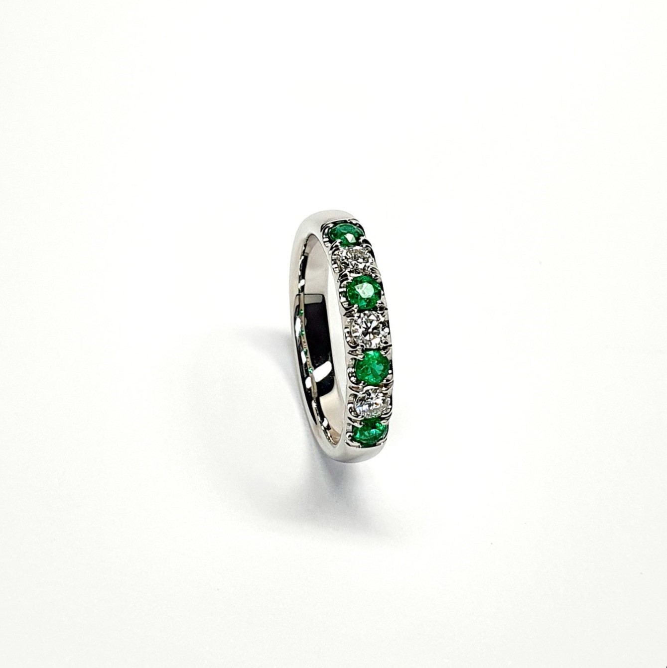 18ct White Gold Emerald & Diamond Eternity Ring RA00685 Four 2.8mm round emeralds and three 2.8mm round diamonds ring standing up to the front angled facing to the right. With a white background.