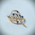 9ct yellow gold brooch with a sprig of seven leaves coming through a floral swirl of polished and barked yellow gold with three diamonds set into a small white rhodium section 