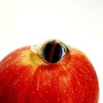 The City of London Jewellers presents the Eyemouth heavy 9ct yellow gold 12mm x 10mm oval Tigers Eye with a slightly curved top rub-over set into a plain polished signet ring, angled view laying down from the front sitting on an apple.