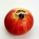 The City of London Jewellers presents the Eyemouth heavy 9ct yellow gold 12mm x 10mm oval Tigers Eye with a slightly curved top rub-over set into a plain polished signet ring, angled view laying down from the front sitting on an apple slight angle from above.