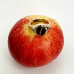 The City of London Jewellers presents the Eyemouth heavy 9ct yellow gold 12mm x 10mm oval Tigers Eye with a slightly curved top rub-over set into a plain polished signet ring, angled view laying down from the front sitting on an apple slight angle from above.