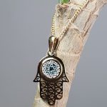 9ct yellow gold filigree style evil eye hamsa pendant and chain/necklace pendant height, including saddle bail 23.6mm width 12.5mm evil-eye set with a single black CZ pupil surrounded with six blue CZs and twelve white CZs.