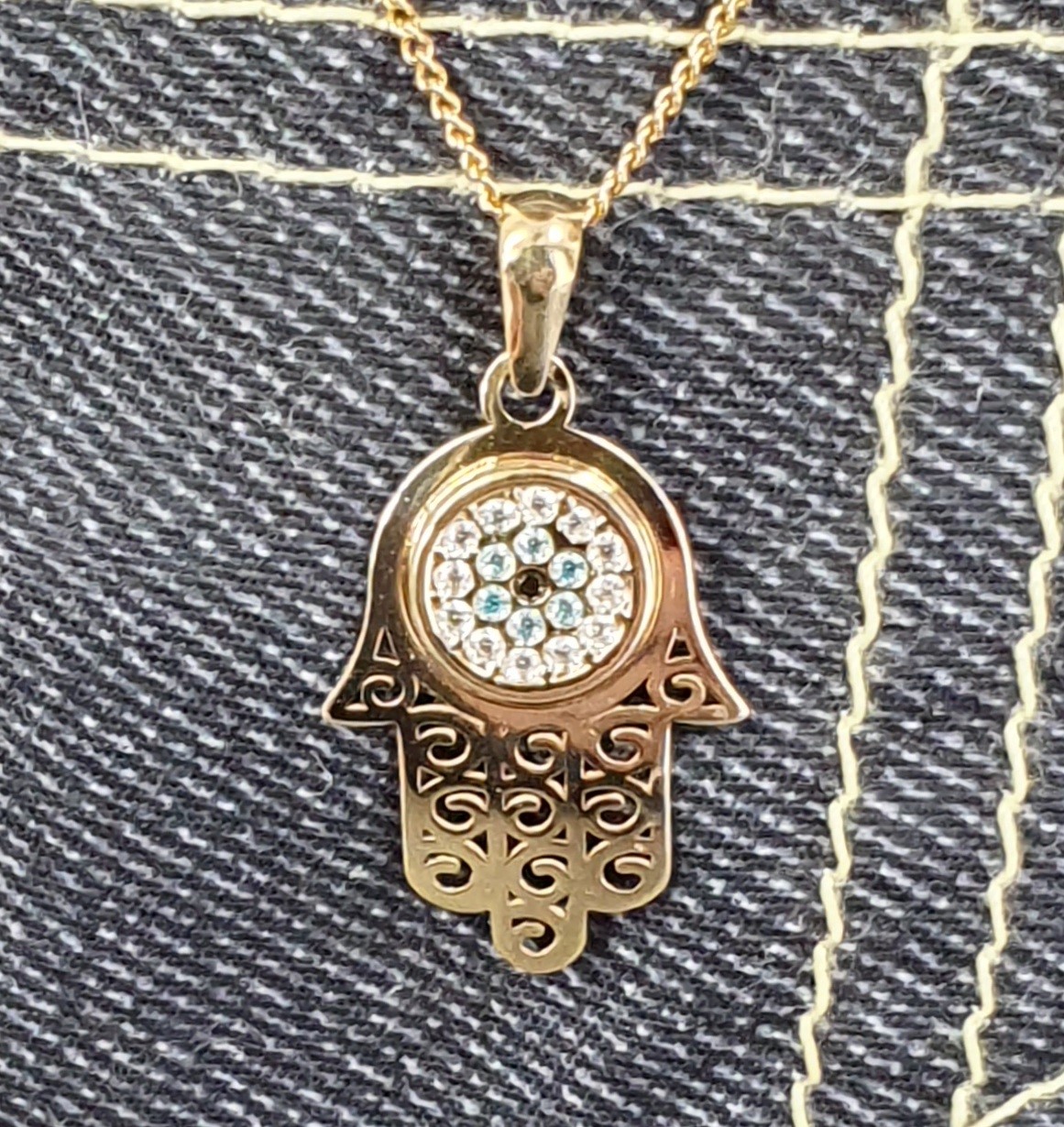 9ct yellow gold filigree style evil eye hamsa pendant and chain/necklace pendant height, including saddle bail 23.6mm width 12.5mm evil-eye set with a single black CZ pupil surrounded with six blue CZs and twelve white CZs.