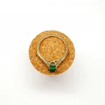 Step cut Emerald Ring with Diamonds to Each Side laying flat on a cork