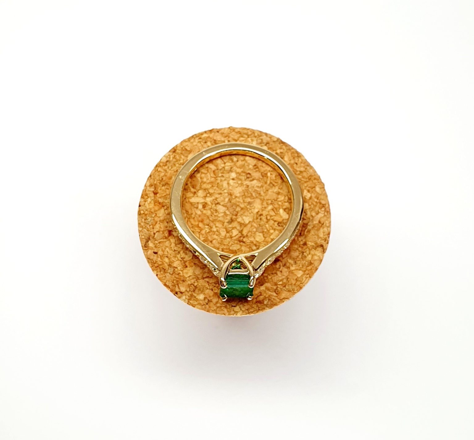 Step cut Emerald Ring with Diamonds to Each Side laying flat on a cork