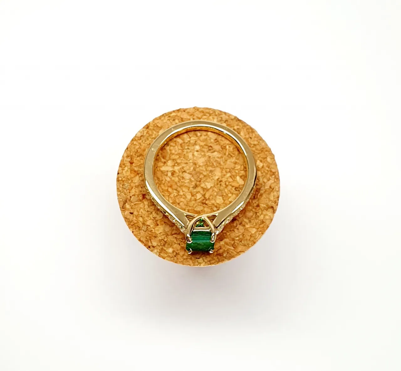 Step cut Emerald Ring with Diamonds to Each Side laying flat on a cork
