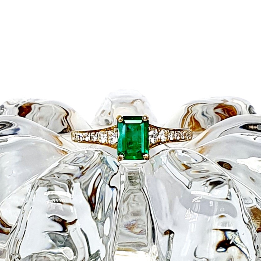Emerald ring on glass surface resembling ice, with cool-toned reflections