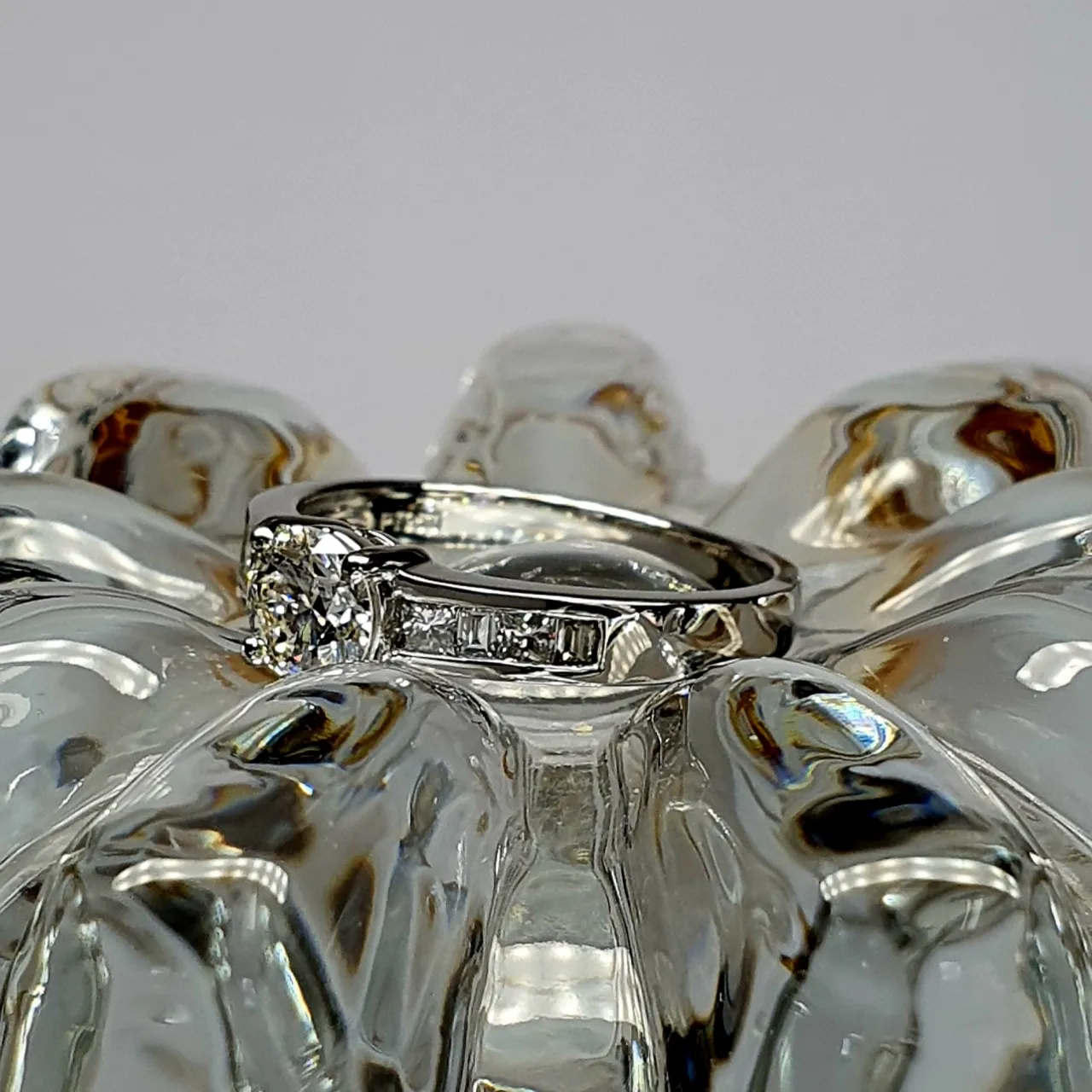 The Lambeth Platinum Diamond Engagement Ring RPT00045 The centre is set with a 0.70ct round brilliant-cut diamond of Colour H clarity SI1, which has an excellent cut, proportions, and symmetry. The side shoulders are channel set with a total of four princess-cut diamonds and four baguette-cut diamonds. The total diamond weight is 1.08 carats.