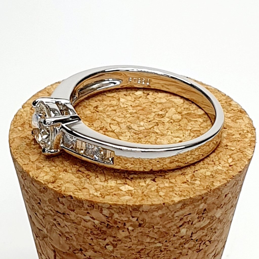 The Lambeth Platinum Diamond Engagement Ring RPT00045 The centre is set with a 0.70ct round brilliant-cut diamond of Colour H clarity SI1, which has an excellent cut, proportions, and symmetry. The side shoulders are channel set with a total of four princess-cut diamonds and four baguette-cut diamonds. The total diamond weight is 1.08 carats.