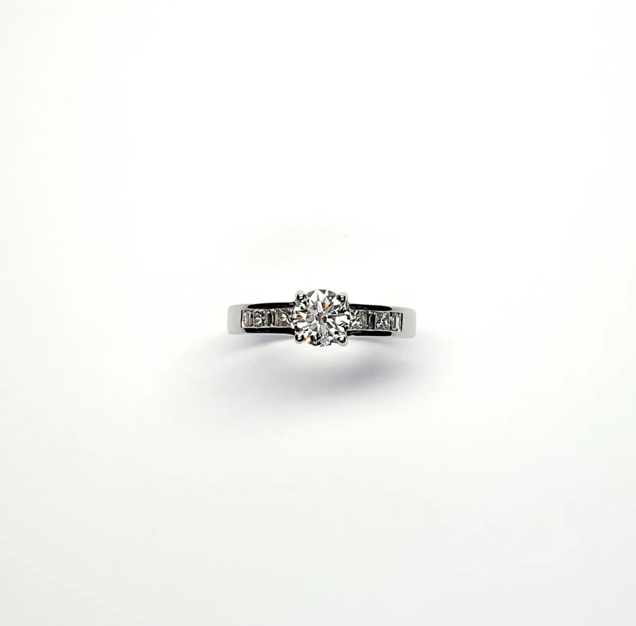 The Lambeth Platinum Diamond Engagement Ring RPT00045 The centre is set with a 0.70ct round brilliant-cut diamond of Colour H clarity SI1, which has an excellent cut, proportions, and symmetry. The side shoulders are channel set with a total of four princess-cut diamonds and four baguette-cut diamonds. The total diamond weight is 1.08 carats.
