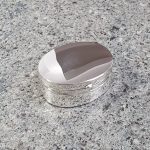 Plain polished oval genuine silver pill/trinket box pictured closed sitting on granite surface.