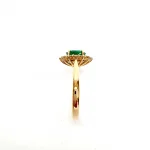 At the heart of this exquisite 18ct yellow gold ring lies a resplendent 7mm x 5mm oval emerald weighing an impressive 0.84 carats and exuding an enchanting green hue. Its captivating charm captures the essence of nature's beauty, with twelve dazzling round brilliant-cut diamonds, totalling 0.41 carats, surrounding the emerald. Each stone is meticulously selected to enhance the ring's allure with unparalleled radiance and brilliance, and the basket-wire setting measures 13mm x 10mm.RA00696.