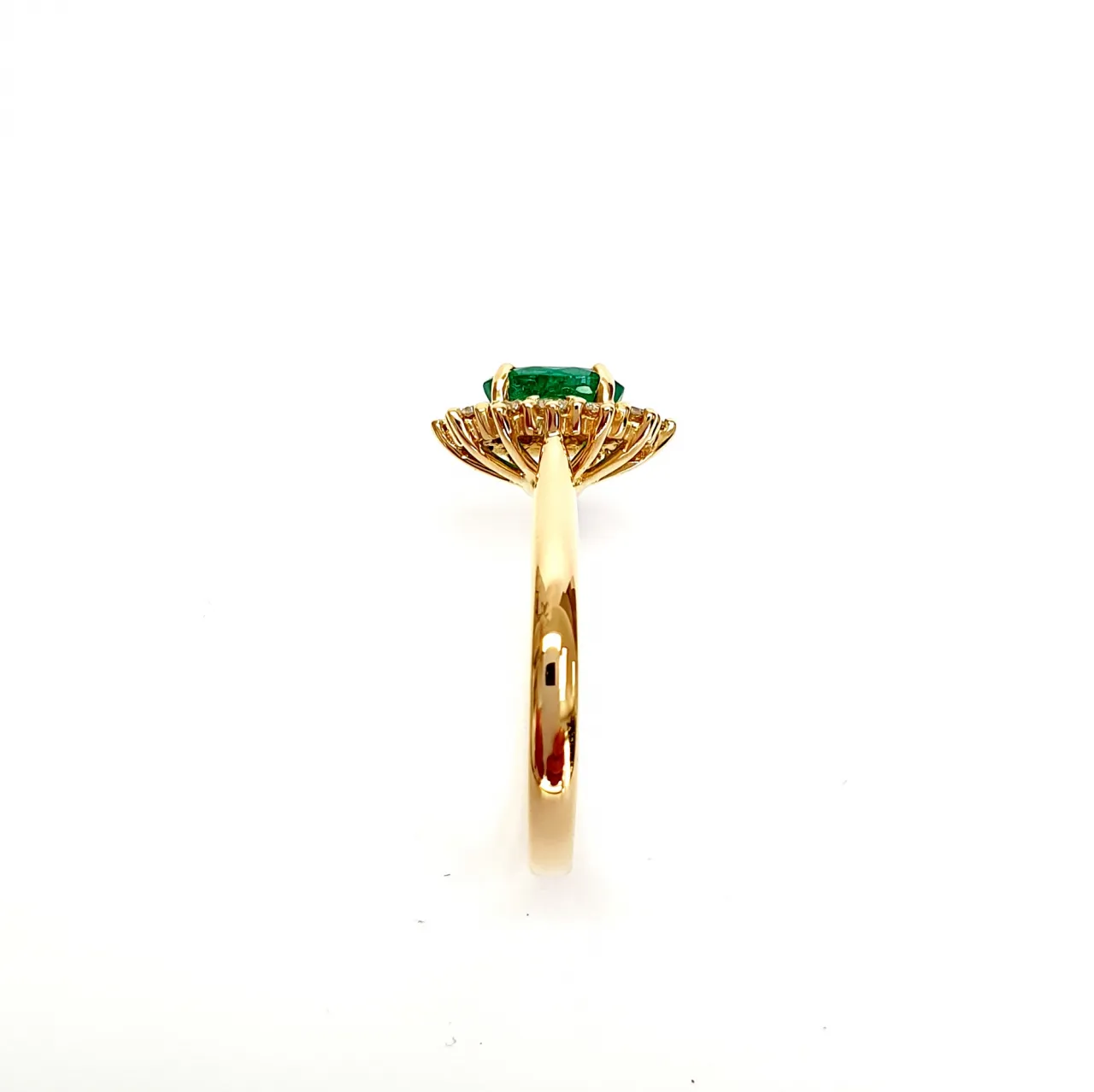 At the heart of this exquisite 18ct yellow gold ring lies a resplendent 7mm x 5mm oval emerald weighing an impressive 0.84 carats and exuding an enchanting green hue. Its captivating charm captures the essence of nature's beauty, with twelve dazzling round brilliant-cut diamonds, totalling 0.41 carats, surrounding the emerald. Each stone is meticulously selected to enhance the ring's allure with unparalleled radiance and brilliance, and the basket-wire setting measures 13mm x 10mm.RA00696.