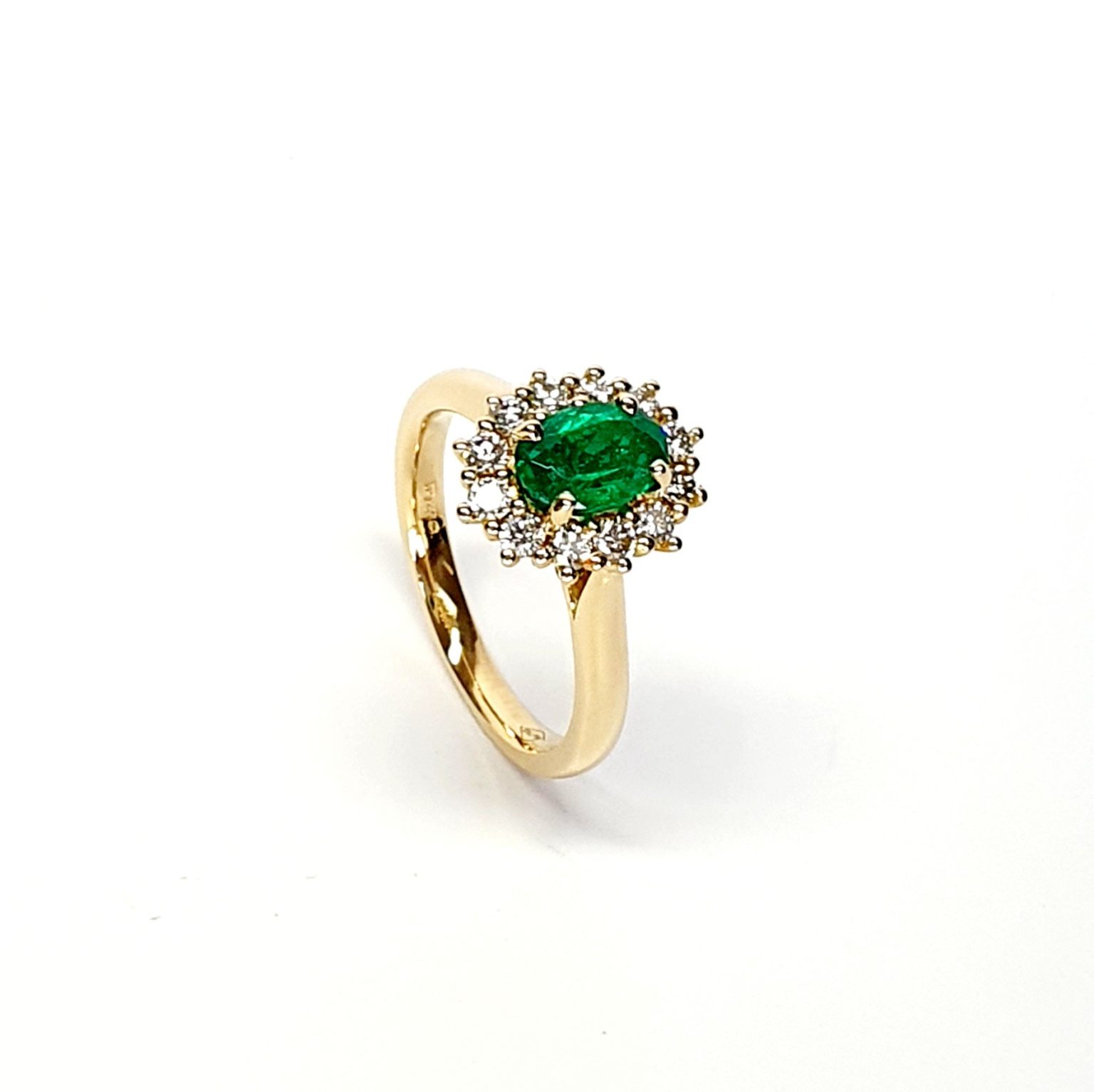 At the heart of this exquisite 18ct yellow gold ring lies a resplendent 7mm x 5mm oval emerald weighing an impressive 0.84 carats and exuding an enchanting green hue. Its captivating charm captures the essence of nature's beauty, with twelve dazzling round brilliant-cut diamonds, totalling 0.41 carats, surrounding the emerald. Each stone is meticulously selected to enhance the ring's allure with unparalleled radiance and brilliance, and the basket-wire setting measures 13mm x 10mm.RA00696.