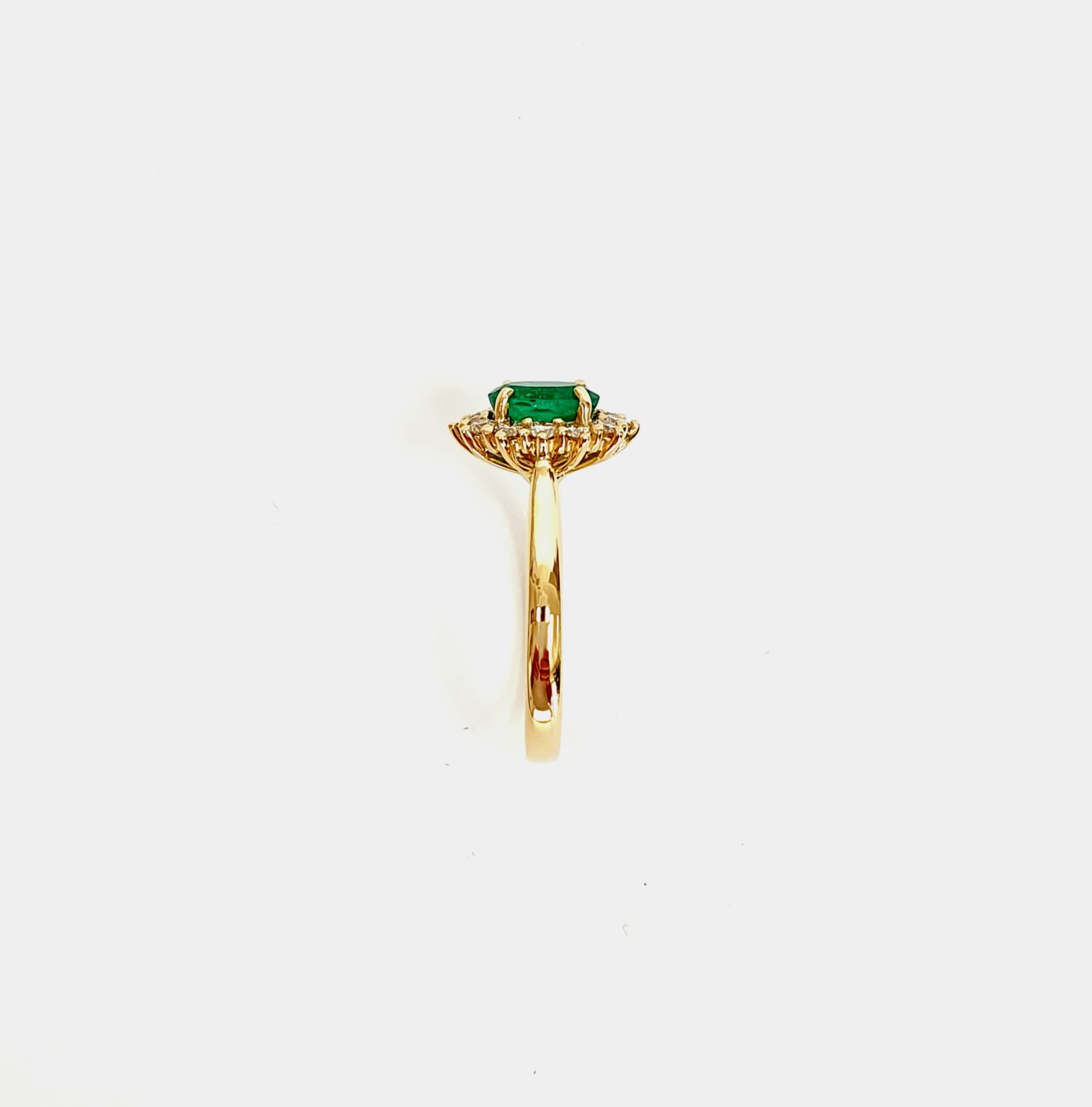 At the heart of this exquisite 18ct yellow gold ring lies a resplendent 7mm x 5mm oval emerald weighing an impressive 0.84 carats and exuding an enchanting green hue. Its captivating charm captures the essence of nature's beauty, with twelve dazzling round brilliant-cut diamonds, totalling 0.41 carats, surrounding the emerald. Each stone is meticulously selected to enhance the ring's allure with unparalleled radiance and brilliance, and the basket-wire setting measures 13mm x 10mm.RA00696.