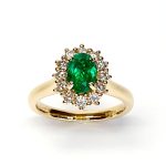 At the heart of this exquisite 18ct yellow gold ring lies a resplendent 7mm x 5mm oval emerald weighing an impressive 0.84 carats and exuding an enchanting green hue. Its captivating charm captures the essence of nature's beauty, with twelve dazzling round brilliant-cut diamonds, totalling 0.41 carats, surrounding the emerald. Each stone is meticulously selected to enhance the ring's allure with unparalleled radiance and brilliance, and the basket-wire setting measures 13mm x 10mm.RA00696.