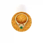 At the heart of this exquisite 18ct yellow gold ring lies a resplendent 7mm x 5mm oval emerald weighing an impressive 0.84 carats and exuding an enchanting green hue. Its captivating charm captures the essence of nature's beauty, with twelve dazzling round brilliant-cut diamonds, totalling 0.41 carats, surrounding the emerald. Each stone is meticulously selected to enhance the ring's allure with unparalleled radiance and brilliance, and the basket-wire setting measures 13mm x 10mm.RA00696.
