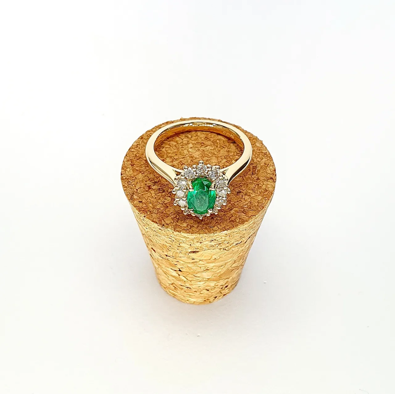 At the heart of this exquisite 18ct yellow gold ring lies a resplendent 7mm x 5mm oval emerald weighing an impressive 0.84 carats and exuding an enchanting green hue. Its captivating charm captures the essence of nature's beauty, with twelve dazzling round brilliant-cut diamonds, totalling 0.41 carats, surrounding the emerald. Each stone is meticulously selected to enhance the ring's allure with unparalleled radiance and brilliance, and the basket-wire setting measures 13mm x 10mm.RA00696.