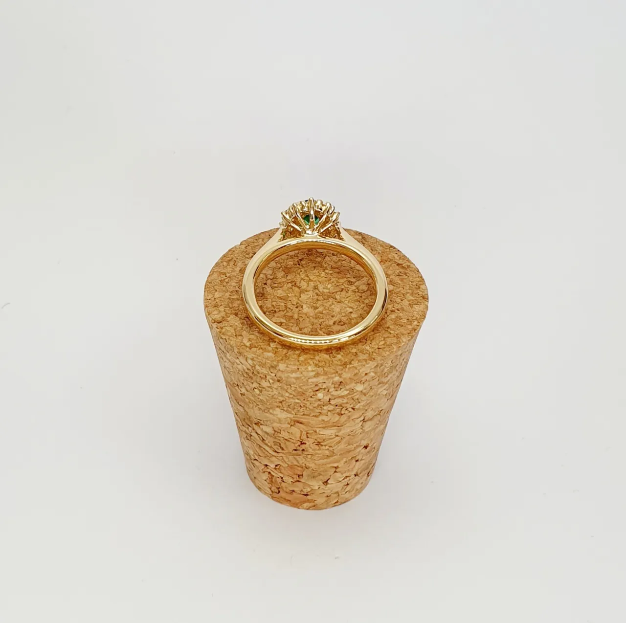 At the heart of this exquisite 18ct yellow gold ring lies a resplendent 7mm x 5mm oval emerald weighing an impressive 0.84 carats and exuding an enchanting green hue. Its captivating charm captures the essence of nature's beauty, with twelve dazzling round brilliant-cut diamonds, totalling 0.41 carats, surrounding the emerald. Each stone is meticulously selected to enhance the ring's allure with unparalleled radiance and brilliance, and the basket-wire setting measures 13mm x 10mm.RA00696.