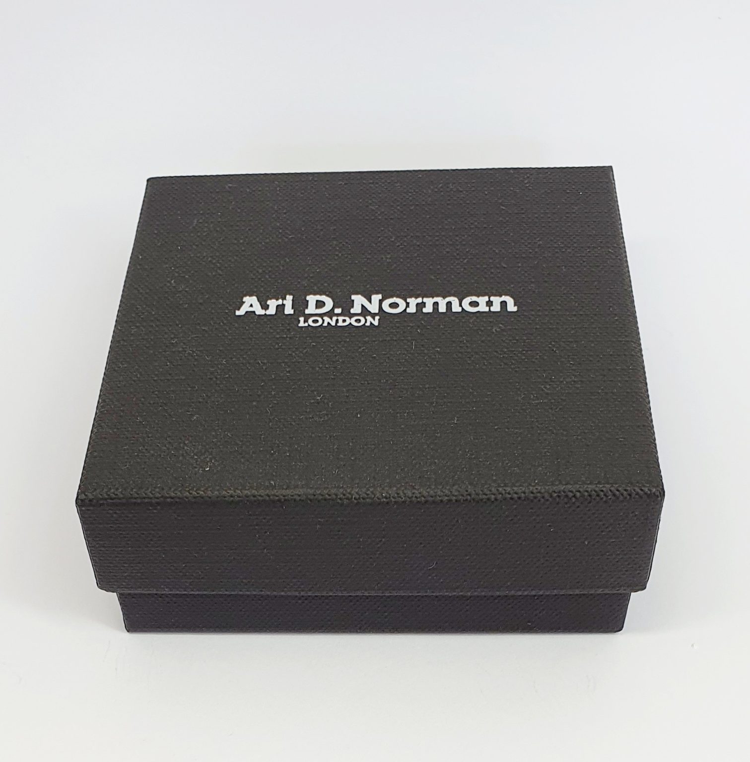 Black cardboard two part box with a black draw string pouch inside. closed.