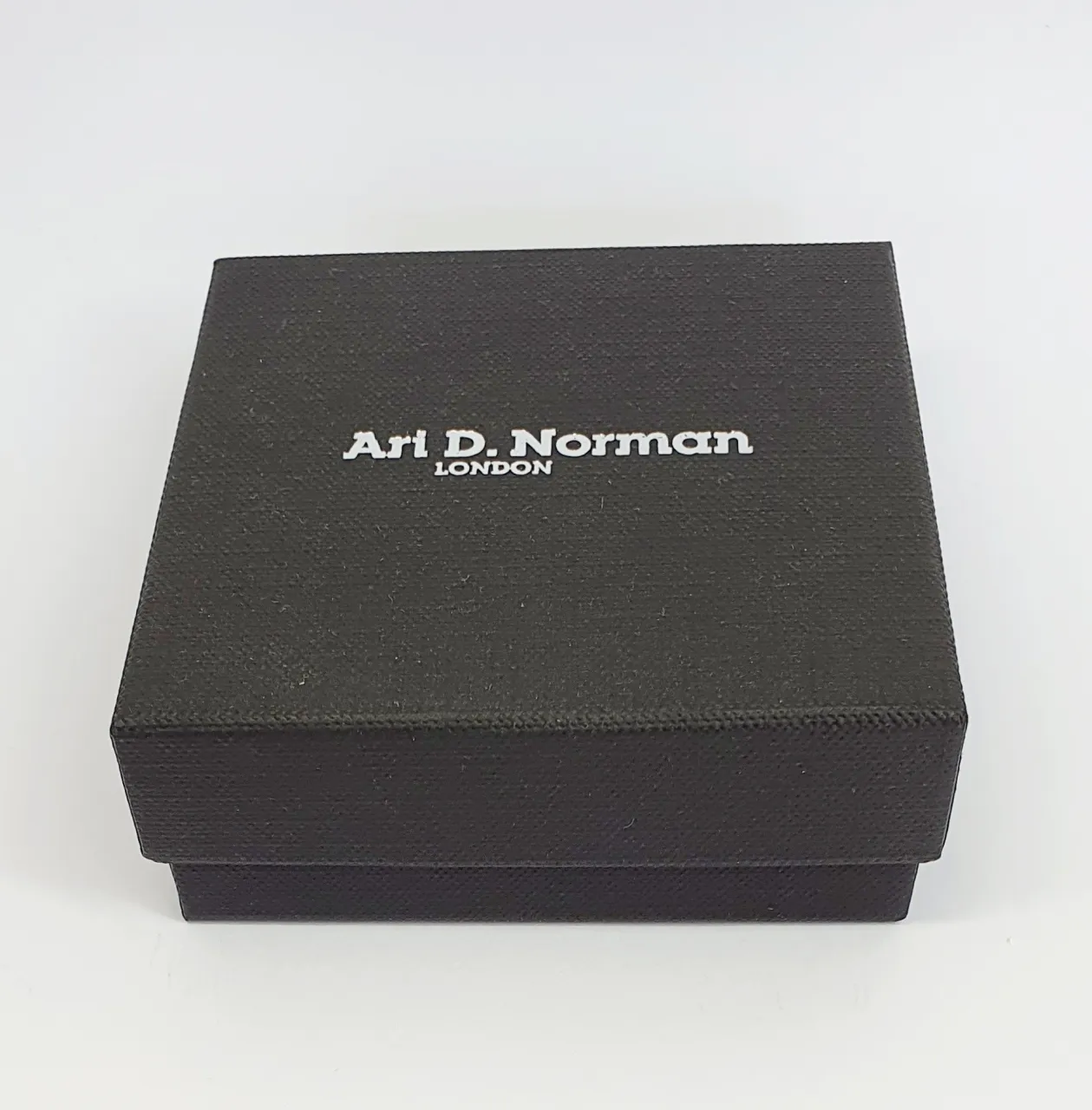 Black cardboard two part box with a black draw string pouch inside. closed.