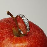 Apple Charm: Resting against the vibrant red of an apple, the ring's step design and dazzling nine graduating princess cut diamonds stones shine beautifully, symbolizing elegance and sophistication.