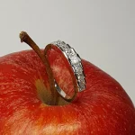 Apple Charm: Resting against the vibrant red of an apple, the ring's step design and dazzling nine graduating princess cut diamonds stones shine beautifully, symbolizing elegance and sophistication.